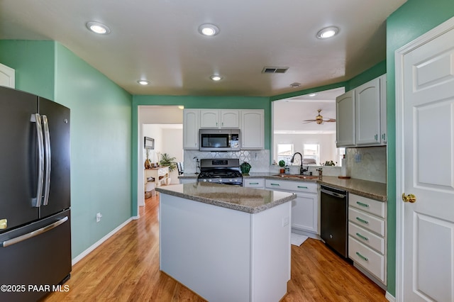 kitchen featuring light wood finished floors, backsplash, appliances with stainless steel finishes, and a sink