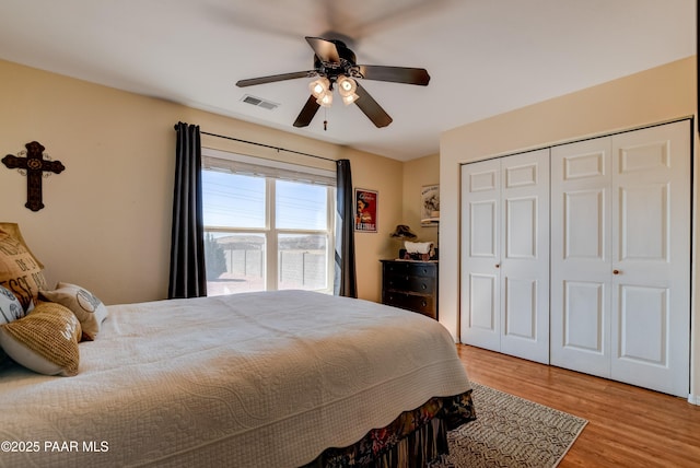 bedroom with light wood-type flooring, visible vents, a closet, and ceiling fan