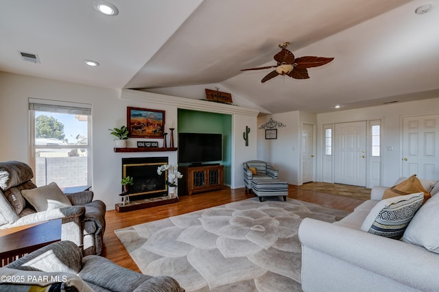 living area featuring visible vents, a fireplace with raised hearth, lofted ceiling, recessed lighting, and wood finished floors