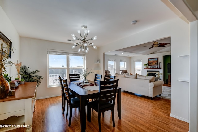 dining room featuring a glass covered fireplace, ceiling fan with notable chandelier, wood finished floors, and visible vents