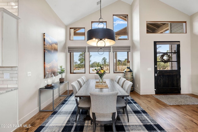 dining area with high vaulted ceiling, a healthy amount of sunlight, and wood finished floors