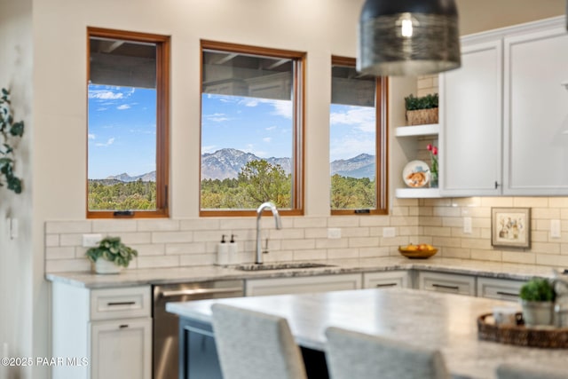 kitchen with white cabinetry, a sink, decorative backsplash, stainless steel dishwasher, and a mountain view