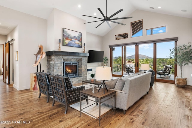 living area with high vaulted ceiling, hardwood / wood-style floors, a barn door, a fireplace, and baseboards