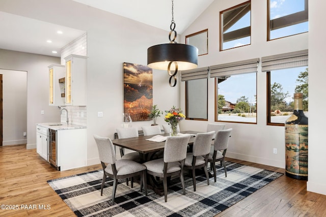 dining room featuring baseboards, wine cooler, recessed lighting, light wood-style floors, and high vaulted ceiling