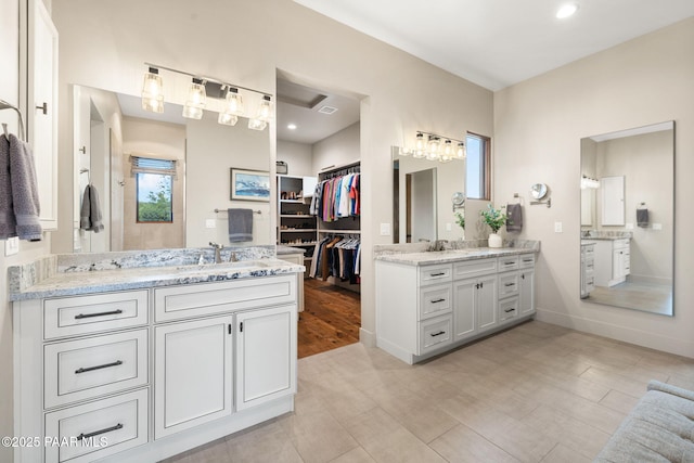 bathroom with a sink, a walk in closet, baseboards, and two vanities