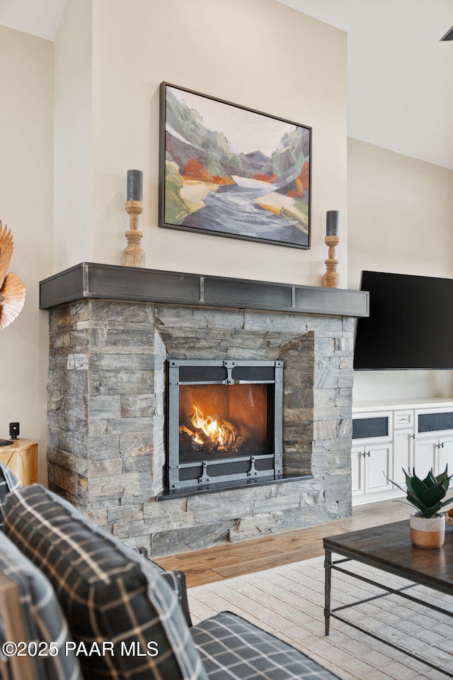 living room featuring lofted ceiling, a stone fireplace, and wood finished floors