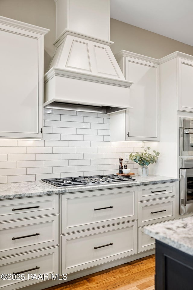 kitchen featuring decorative backsplash, custom exhaust hood, appliances with stainless steel finishes, and white cabinetry