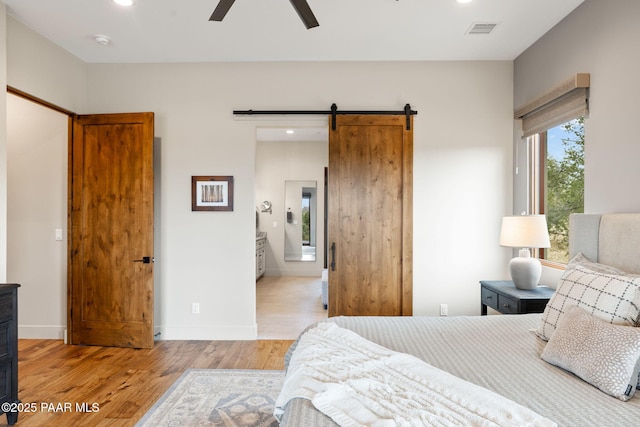 bedroom with a barn door, light wood-style flooring, baseboards, and visible vents