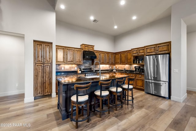 kitchen featuring a high ceiling, a kitchen bar, stainless steel appliances, dark stone countertops, and a center island with sink