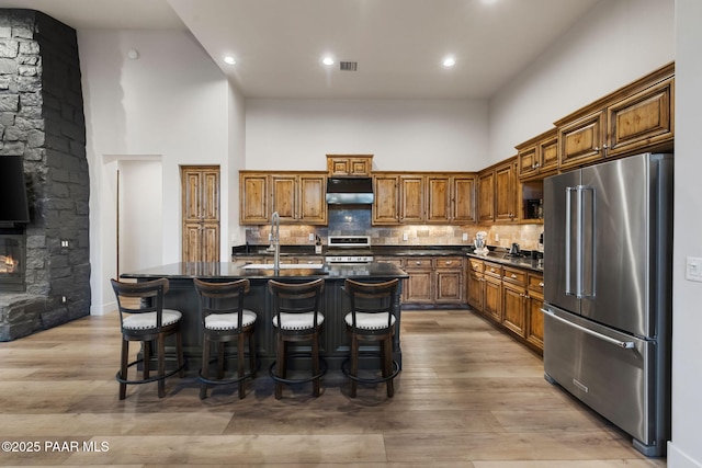 kitchen featuring a high ceiling, stainless steel appliances, decorative backsplash, sink, and a kitchen island with sink