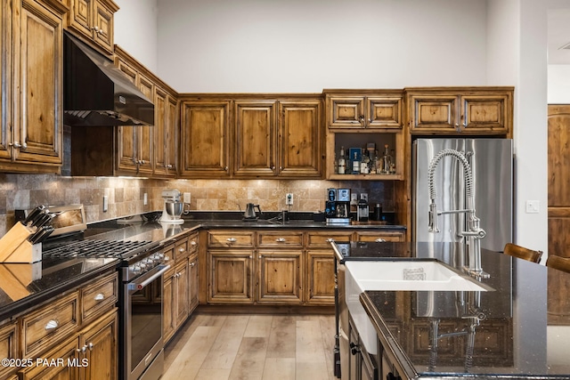 kitchen featuring backsplash, light wood-type flooring, dark stone counters, and stainless steel appliances