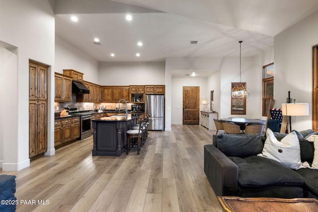 kitchen with appliances with stainless steel finishes, light hardwood / wood-style floors, ventilation hood, a center island with sink, and a breakfast bar area