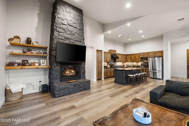 living room featuring a fireplace, a towering ceiling, sink, and light hardwood / wood-style floors