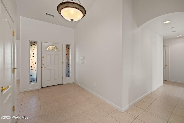 foyer with light tile patterned flooring, arched walkways, visible vents, and baseboards