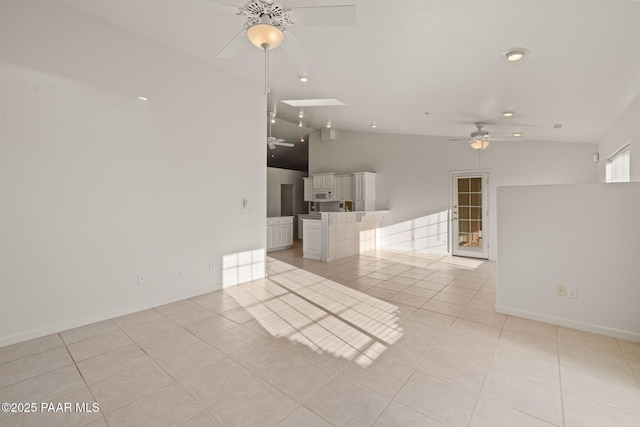 empty room with light tile patterned floors, lofted ceiling with skylight, baseboards, and ceiling fan