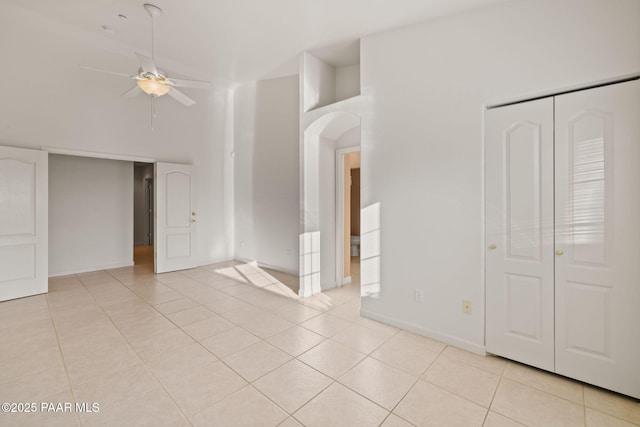 interior space featuring light tile patterned floors, a ceiling fan, baseboards, arched walkways, and a towering ceiling