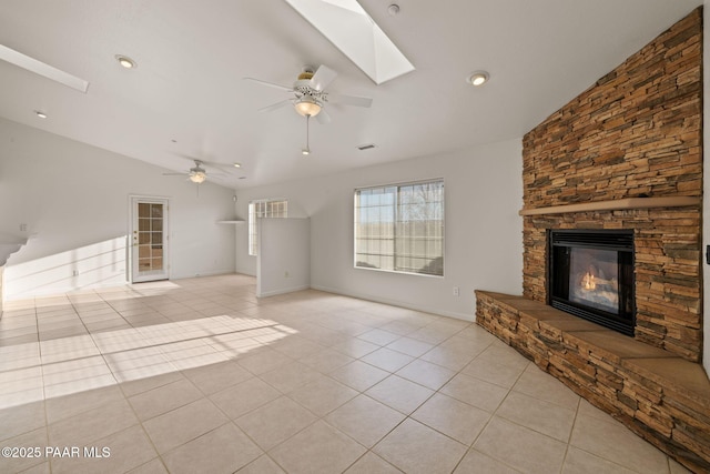 unfurnished living room featuring light tile patterned floors, visible vents, vaulted ceiling with skylight, ceiling fan, and a stone fireplace