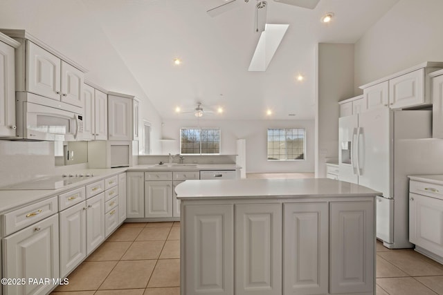 kitchen featuring white appliances, vaulted ceiling with skylight, a center island, and light countertops