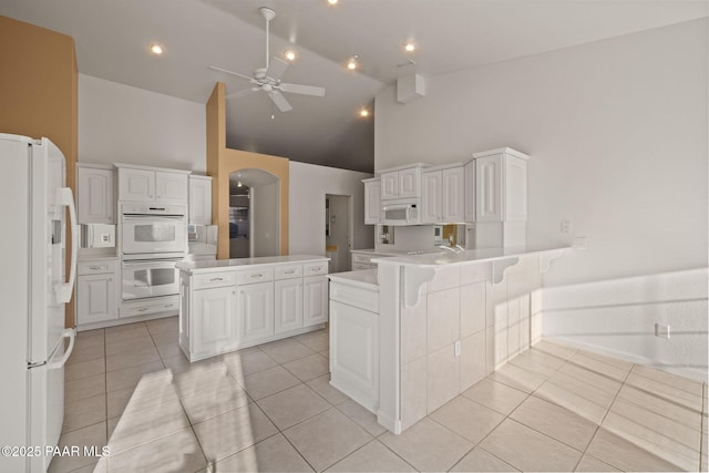 kitchen featuring light tile patterned floors, white cabinets, white appliances, and a peninsula