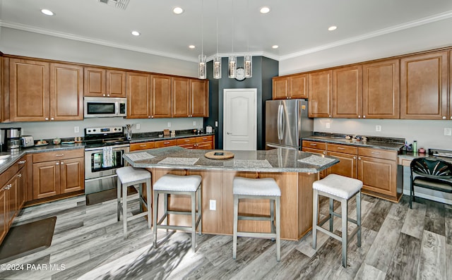 kitchen with appliances with stainless steel finishes, a kitchen breakfast bar, crown molding, light hardwood / wood-style flooring, and a center island