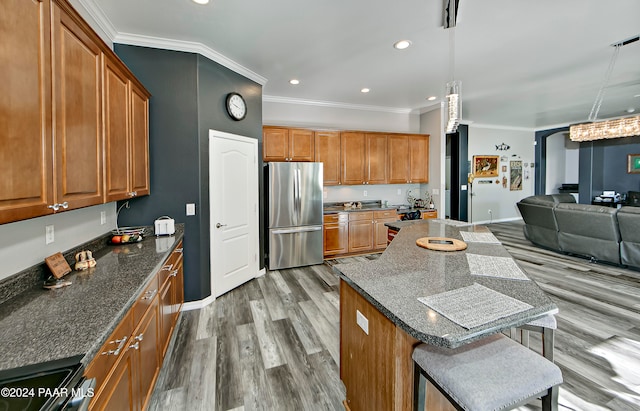 kitchen with stainless steel fridge, ornamental molding, pendant lighting, hardwood / wood-style flooring, and a breakfast bar area