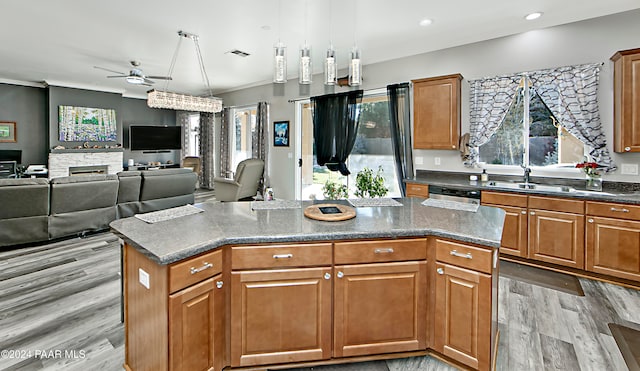 kitchen featuring sink, a stone fireplace, light hardwood / wood-style flooring, an island with sink, and decorative light fixtures