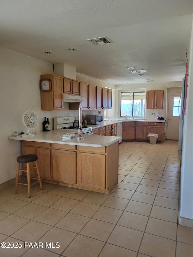 kitchen featuring light tile patterned flooring, a breakfast bar, sink, kitchen peninsula, and white appliances