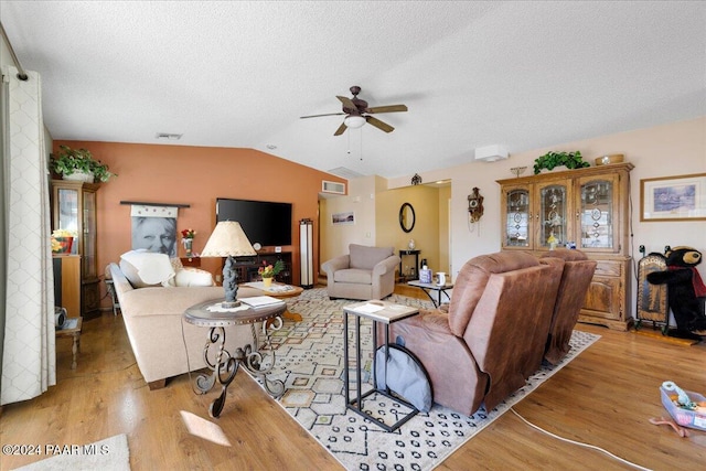 living room with ceiling fan, light wood-type flooring, a textured ceiling, and vaulted ceiling