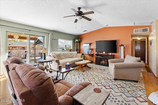 living room featuring ceiling fan, light hardwood / wood-style floors, lofted ceiling, and a textured ceiling