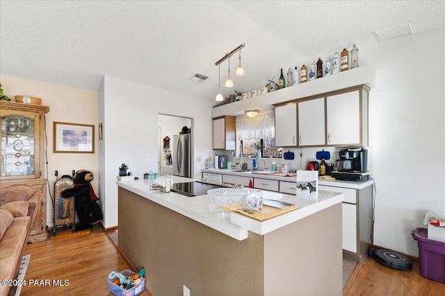 kitchen with a textured ceiling, decorative light fixtures, a center island, light hardwood / wood-style floors, and stainless steel refrigerator