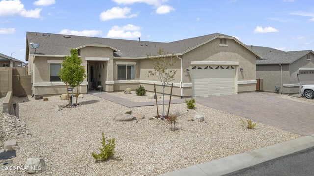 ranch-style home featuring decorative driveway, a garage, stucco siding, and roof with shingles