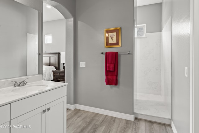 ensuite bathroom featuring connected bathroom, vanity, a shower, baseboards, and wood finished floors