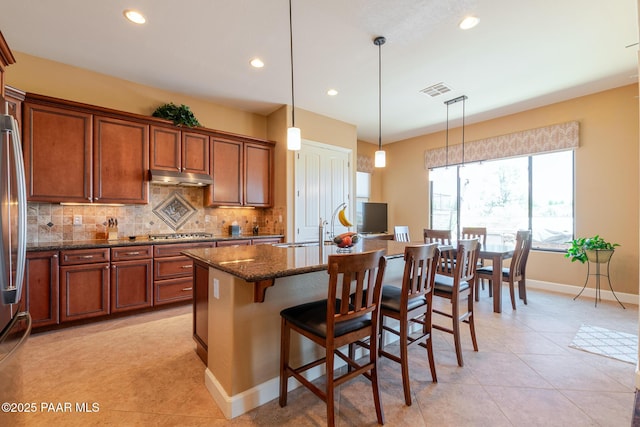 1646 Constable St, Prescott, AZ 86301 - kitchen featuring under cabinet range hood, backsplash, appliances with stainless steel finishes, light tile patterned floors, and dark stone countertops