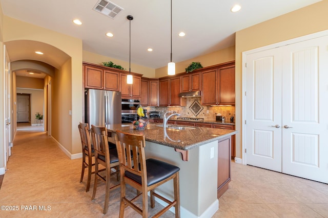 1646 Constable St, Prescott, AZ 86301 - kitchen featuring brown cabinets, decorative backsplash, dark stone counters, an island with sink, and a kitchen bar