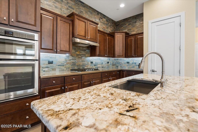 kitchen with stainless steel appliances, light stone countertops, sink, and backsplash