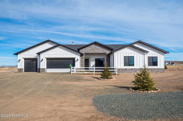 modern farmhouse style home featuring board and batten siding, stone siding, an attached garage, and dirt driveway