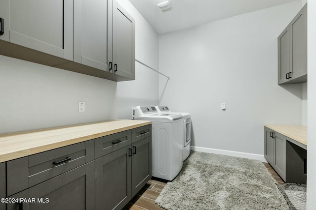 clothes washing area with washer and dryer, cabinets, and wood-type flooring