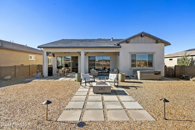 rear view of property featuring a jacuzzi, a patio, and an outdoor living space with a fire pit