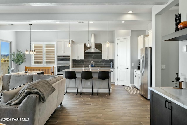 kitchen featuring white cabinetry, wall chimney exhaust hood, hanging light fixtures, and appliances with stainless steel finishes