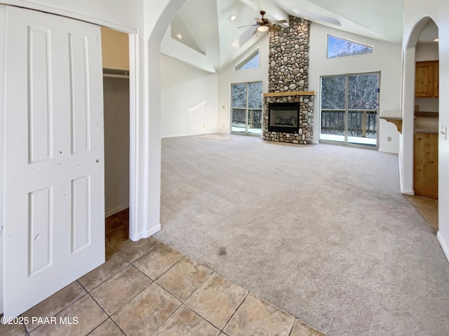 unfurnished living room with ceiling fan, high vaulted ceiling, a fireplace, beamed ceiling, and carpet
