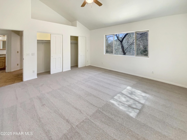 unfurnished bedroom with baseboards, a ceiling fan, carpet floors, high vaulted ceiling, and two closets
