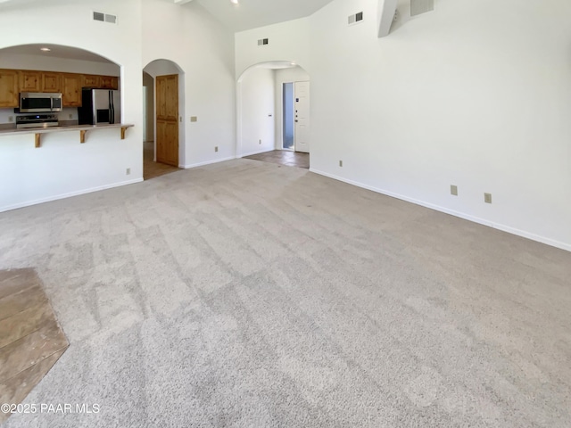 unfurnished living room with high vaulted ceiling, light colored carpet, visible vents, and arched walkways