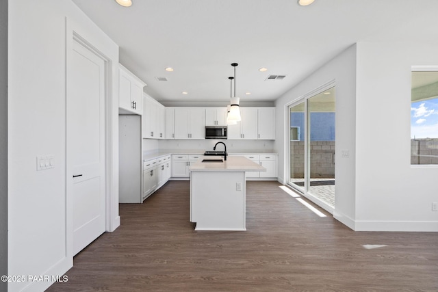 kitchen with white cabinetry, range with electric cooktop, hanging light fixtures, dark hardwood / wood-style flooring, and a center island with sink