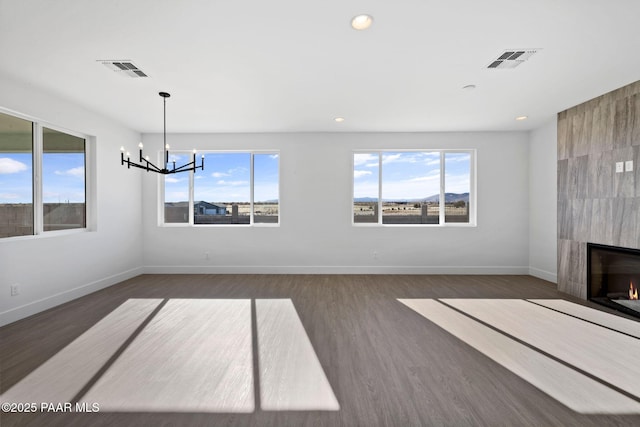 unfurnished living room featuring a healthy amount of sunlight, a fireplace, dark wood-type flooring, and a notable chandelier