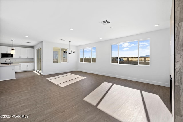 unfurnished living room featuring dark hardwood / wood-style floors, sink, and an inviting chandelier