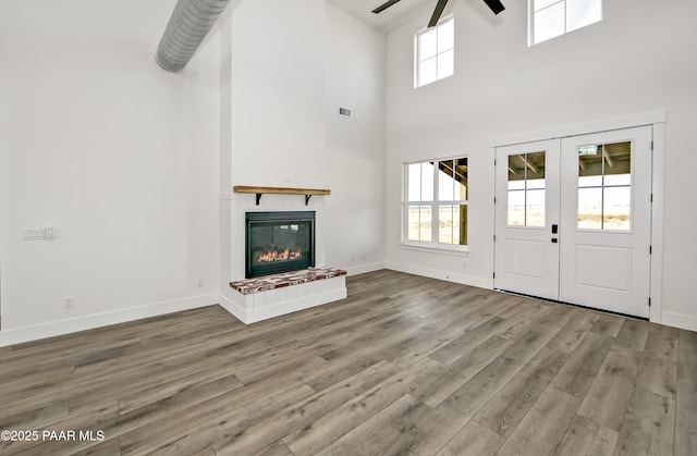 unfurnished living room with a high ceiling, french doors, a fireplace, light hardwood / wood-style floors, and ceiling fan