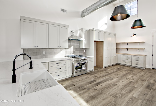 kitchen featuring pendant lighting, white cabinets, high end range, wall chimney exhaust hood, and decorative backsplash