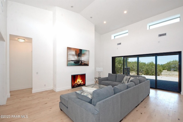 living area featuring high vaulted ceiling, light wood-type flooring, visible vents, and a lit fireplace