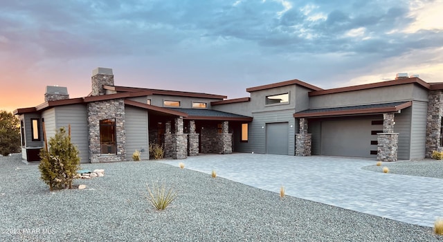 view of front of house with an attached garage, stone siding, a chimney, and decorative driveway