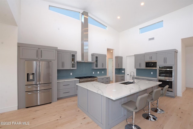 kitchen with light stone counters, gray cabinetry, a sink, appliances with stainless steel finishes, and light wood-type flooring